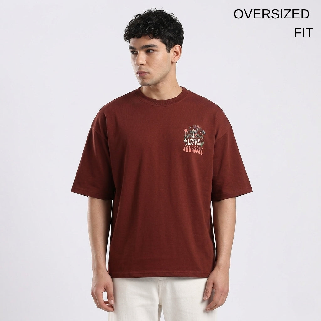 Man wearing an oversized maroon t-shirt with a graphic design on a white background