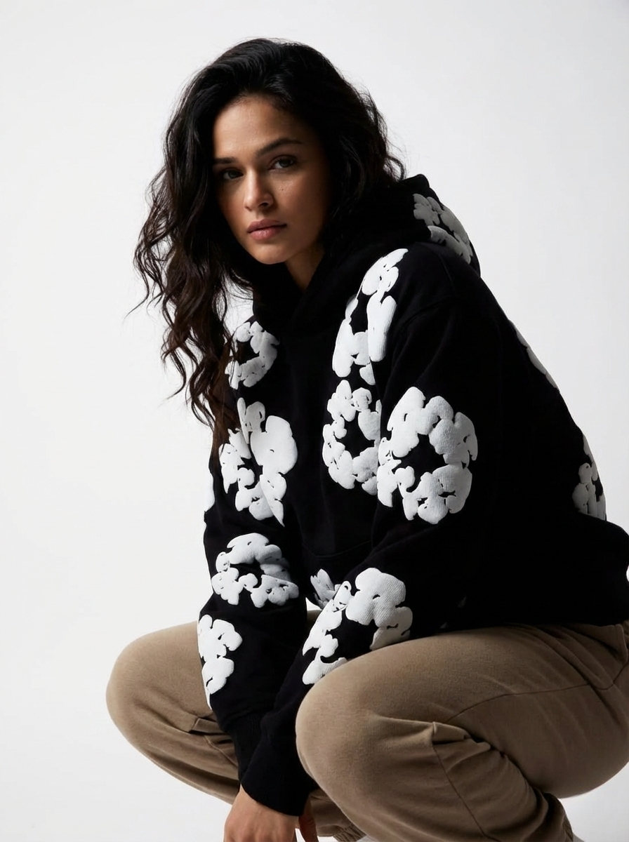 Woman wearing a black hoodie with white floral patterns on a plain background