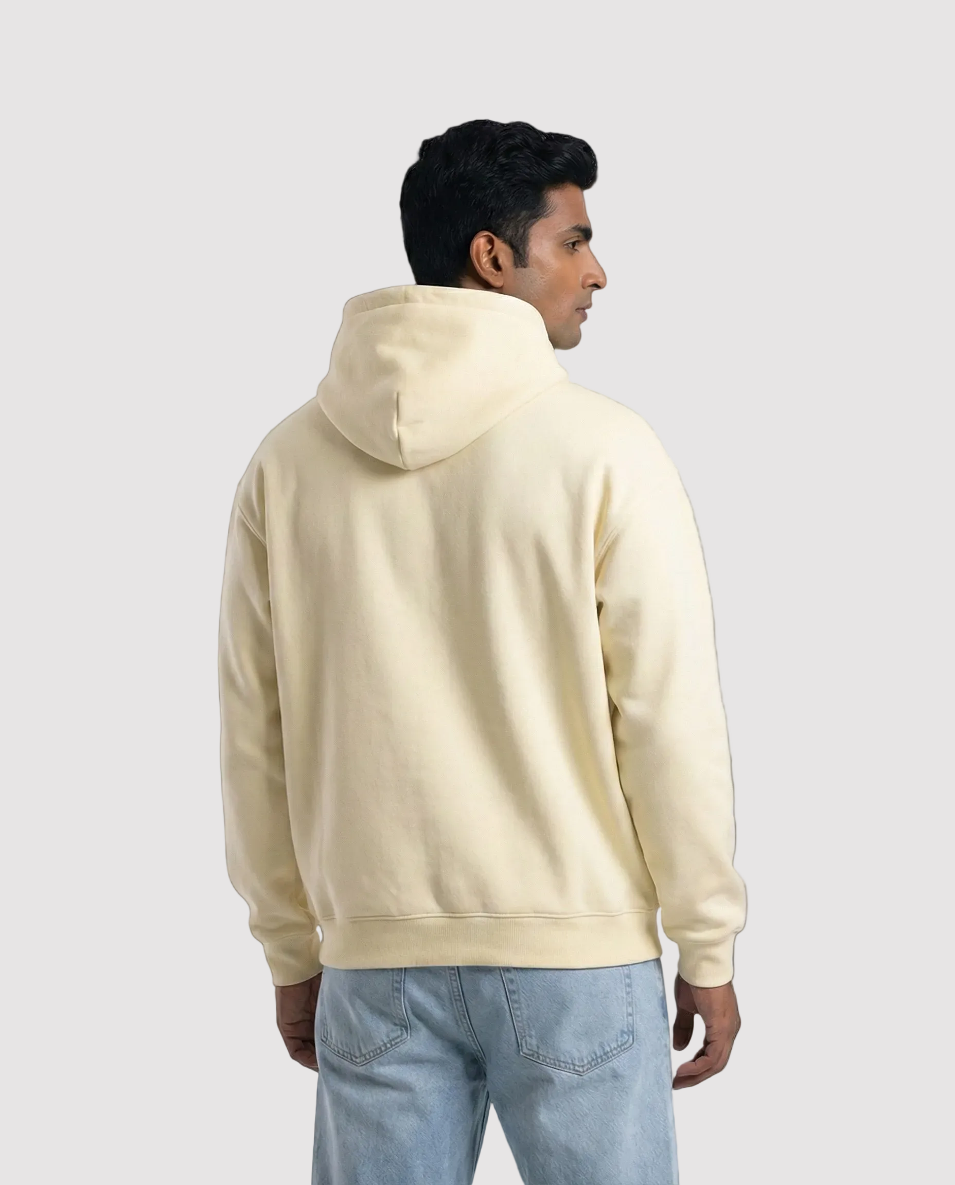 Man wearing a beige hoodie and light blue jeans on a white background