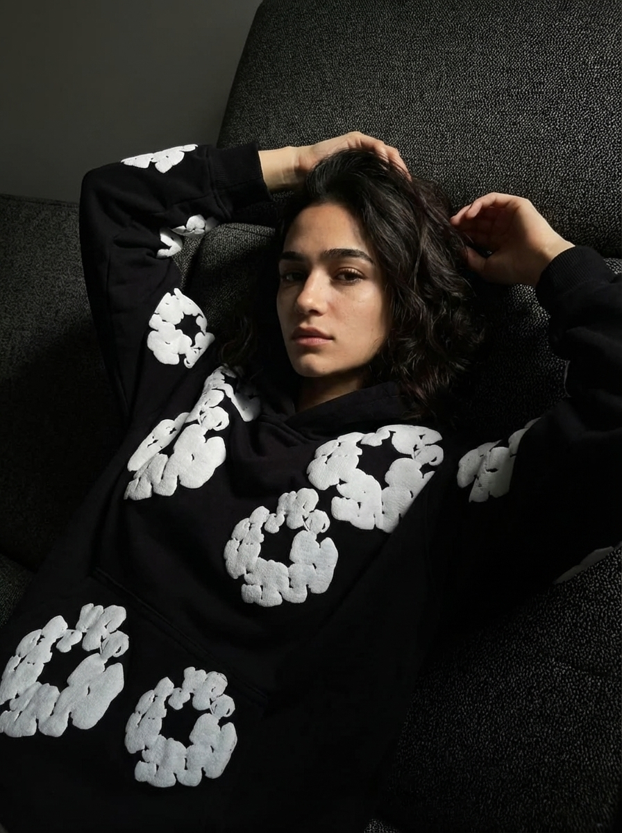 Person wearing a black hoodie with white patterns, sitting on a dark surface.