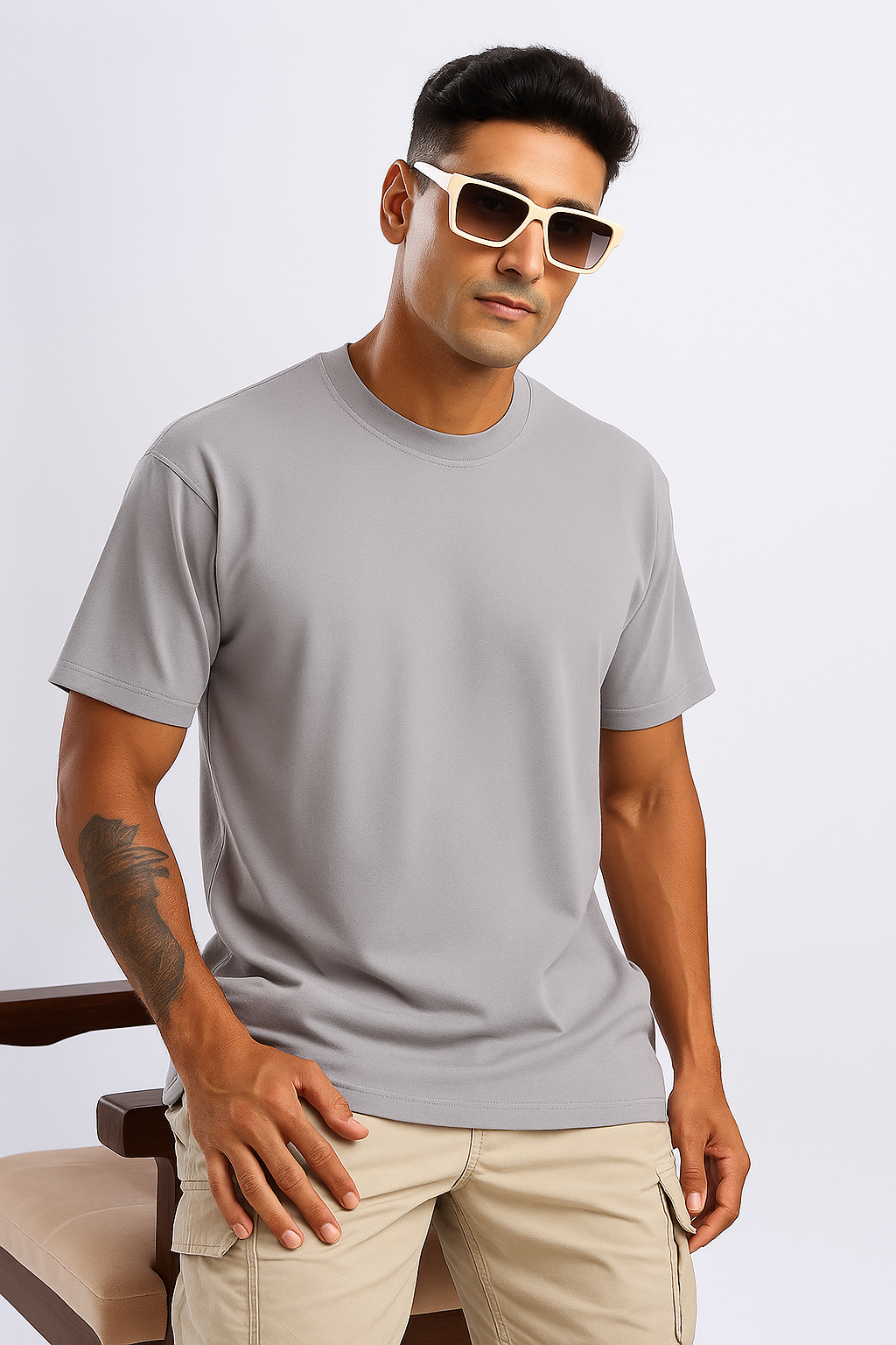 Man wearing a light gray oversized T-shirt and beige cargo pants, seated on a chair in a lifestyle setting.