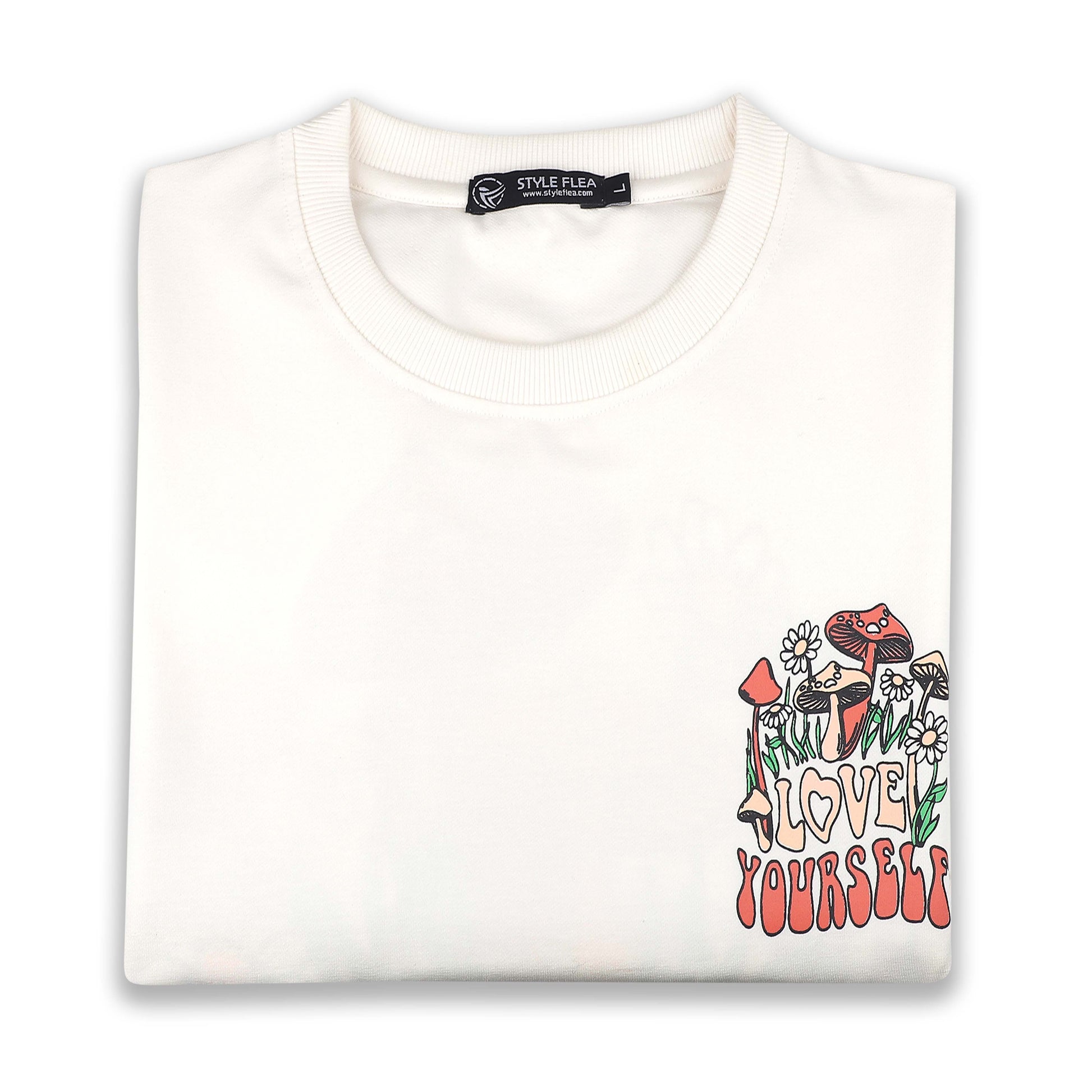 White drop shoulder T-shirt neatly folded, displaying the "Love Yourself" mushroom and floral chest graphic.