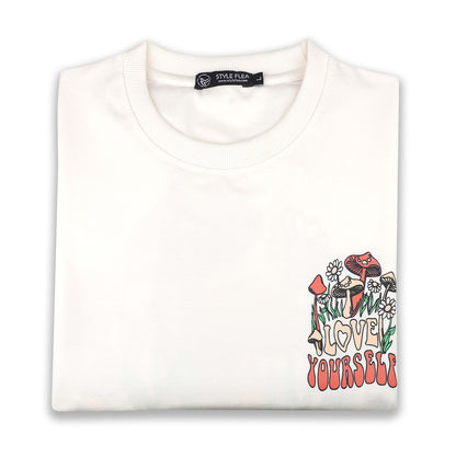 White drop shoulder T-shirt neatly folded, displaying the "Love Yourself" mushroom and floral chest graphic.