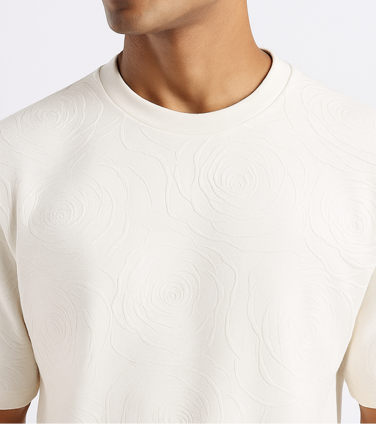 Close-up of a white drop shoulder T-shirt featuring an embossed rose design, highlighting the textured floral detail on the fabric.